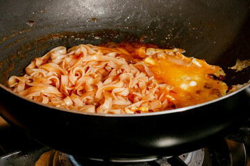 Tangy tomato-infused noodles sizzle in raven-black wok, evoking Lunar New Year flavors and World Pasta Day festivities