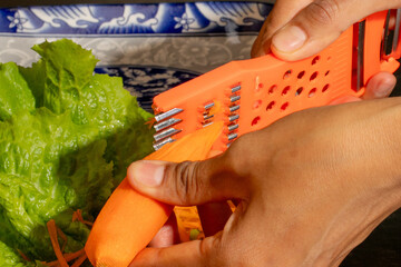 Grating vibrant carrots beside crisp lettuce, a South Asian man's hands evoke Diwalis festive...