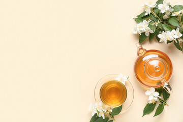 Glass cup and teapot of hot jasmine tea with flowers on beige background
