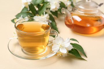 Glass cup and teapot of hot jasmine tea with flowers on beige background, closeup