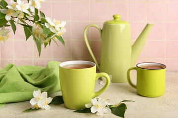 Cups and teapot of hot jasmine tea with flowers on white table