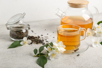Glass cup and teapot of hot jasmine tea with dry leaves on white background