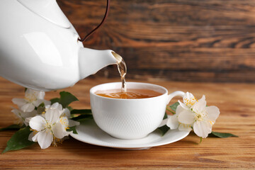 Pouring hot jasmine tea from teapot into cup on wooden background