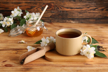 Cup of hot jasmine tea with dry leaves and jar of honey on wooden background