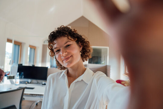 Smiling businesswoman taking selfie in sunny modern office - Powered by Adobe