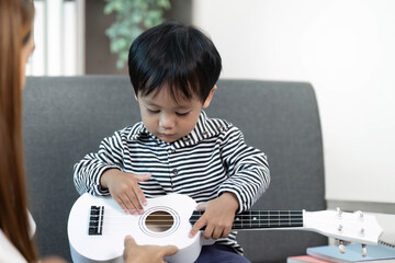 Creative Exploration. Child learning to play a toy guitar with mother's assistance.