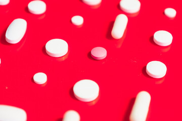 A multitude of white tablets and capsules, along with one pink one, scattered randomly across a...