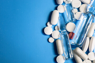 Various white pills, capsules, and transparent ampoules are scattered haphazardly in the bottom...