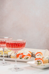 Elegant glasses of red sparkling drink served beside assorted sushi rolls on a white table create a...