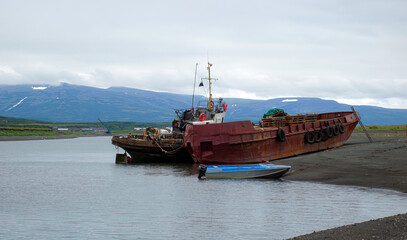 Old fishing boat and barge anchored on shore at low tide. Kamchatka, North