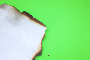A burned sheet of lined paper is placed on a bright green background, creating a distinct visual...