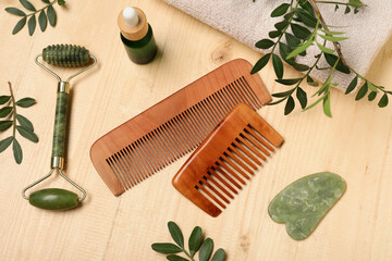 Composition with hair combs, facial massage tools and bottle of cosmetic product on wooden...