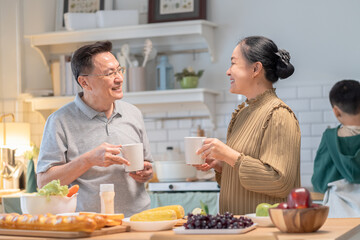 Joyful Asian grandparent, bonding at home lifestyle, warm moment of elderly couple enjoying coffee conversation while grandson stands together, cozy holiday kitchen with relaxed background atmosphere