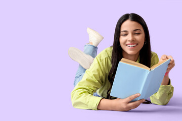 Beautiful woman with book lying on lilac background