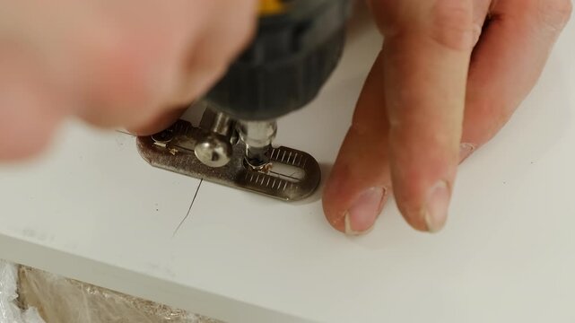 Fixing clip to wooden surface using special professional tool. Furniture assembler installs screws connecting mechanism to material for further stages of assembly