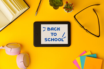 Colorful back to school stationery and digital tablet with cheerful message on bright yellow background