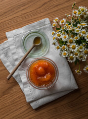 Apricot jam in a glass jar on a wooden table, top view