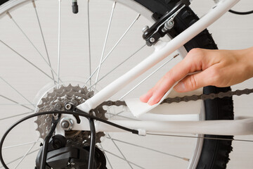 Young adult woman hand holding white dry paper napkin and cleaning bicycle chain on light gray wall background. Closeup. Front view.