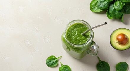 A vibrant green smoothie in a mason jar with spinach leaves and avocado on a light surface