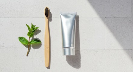 An eco-friendly bamboo toothbrush, a sprig of fresh mint, and a silver toothpaste tube on white tiles