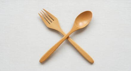 Wooden fork and spoon crossed on a textured white background, highlighting eco-friendly dining