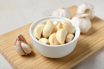Wooden board with fresh garlics and bowl of cloves on white background, closeup