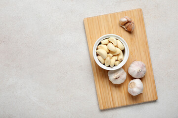 Wooden board with fresh garlics and bowl of cloves on white background