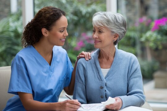 Nurse comforting elderly woman doing crossword puzzle at home
