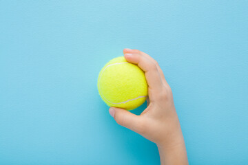Little child boy hand holding and showing new yellow tennis ball on light blue wall background....
