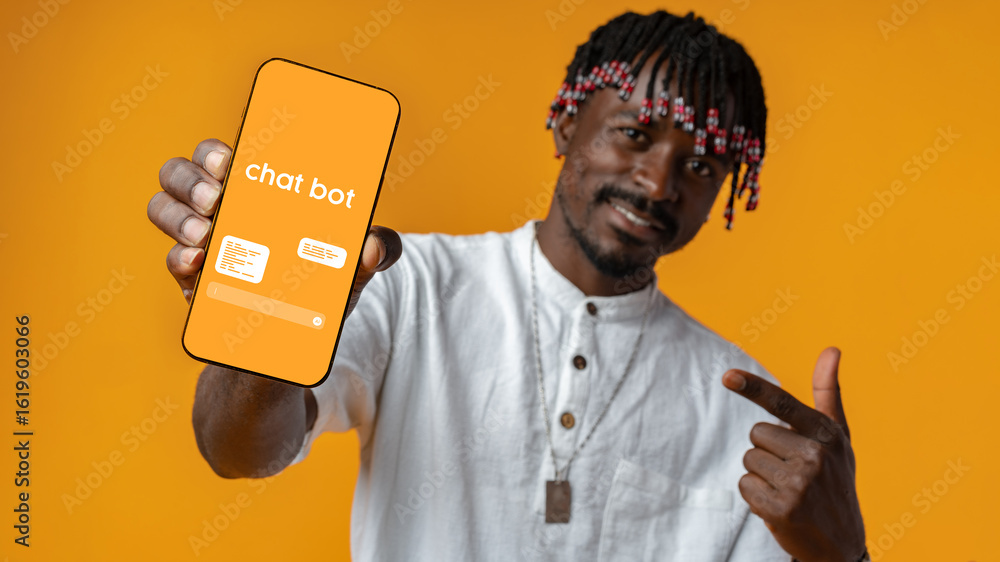 Poster man showcasing chatbot on smartphone against vibrant orange background while smiling and pointing