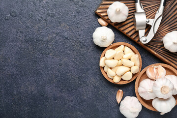 Bowls and wooden board with fresh garlics on dark background