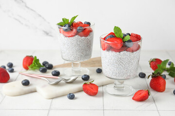 Glasses of tasty chia seed pudding with fresh berries and mint on white tile table