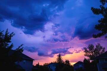 Colorful sunset over residential neighborhood.  Silhouette of houses and trees against dramatic purple and orange clouds