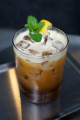 Close up glass of iced Americano coffee decorated with lemon peel and mint leaf on wooden table
