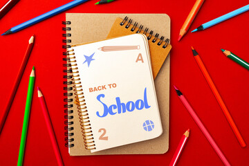 Colorful school supplies arranged on a bright red background, showcasing notebooks and colored...