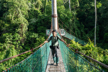 Asian man at suspension bridge in tree top canopy walkway in Danum rain forest Lahad Datu