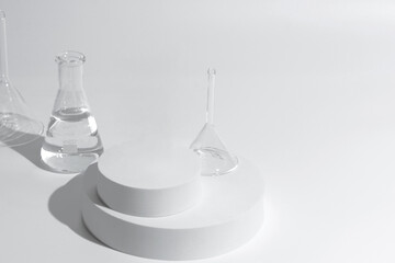 science with transparent glass erlenmeyer flask and funnel and beaker filled with colorless liquid water on a white cylinder base stand on desktop tabletop display with a simple clean background
