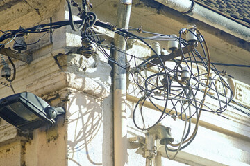 Tangled electric cables and power lines on the side of an old building. Chaotic infrastructure...