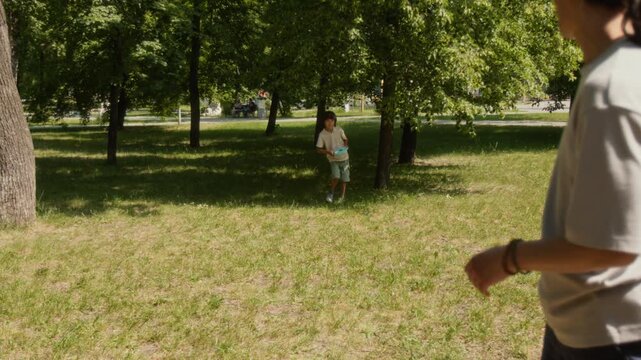 Young man throwing frisbee disk to his son, while spending time together on sunny weekend day in park