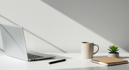 A minimalist home office desk with a laptop, coffee mug, and small plant under bright natural light