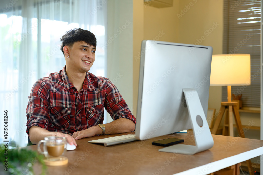 Poster smiling man working on desktop computer in a modern home office with warm lighting