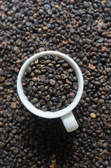 Green coffee beans in a small coffee cup on a background of beans. Alternative drink concept. Selective focus. Vertical orientation. Top view. Copy space