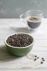 Green coffee beans in a bowl with a glass cup of coffee on a white wooden table. Alternative drink concept. Selective focus. Vertical orientation.