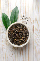Green coffee beans in a bowl with green leaves on a white wooden table. Alternative drink concept. Selective focus. Vertical orientation. Top view