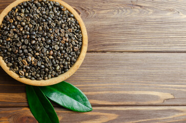 Green coffee beans in a wooden bowl with green leaves on a brown table. Alternative drink concept. Selective focus. Horizontal orientation. Rustic style. Copy space. Top view