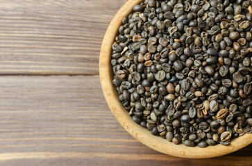 Green coffee beans in a wooden bowl on a brown table. Alternative drink concept. Selective focus. Rustic style. Horizontal orientation. Copy space. Top view