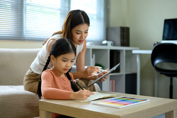 Smiling mom supporting her little girl with schoolwork at home