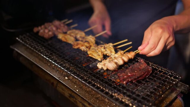 Close up of a chef hands cooking meat Yakitori skewers on a grill at a Japanese restaurant