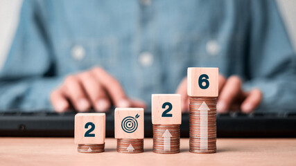 Wooden blocks with numbers 2026 on ascending coin stacks, symbolizing future financial goals,...