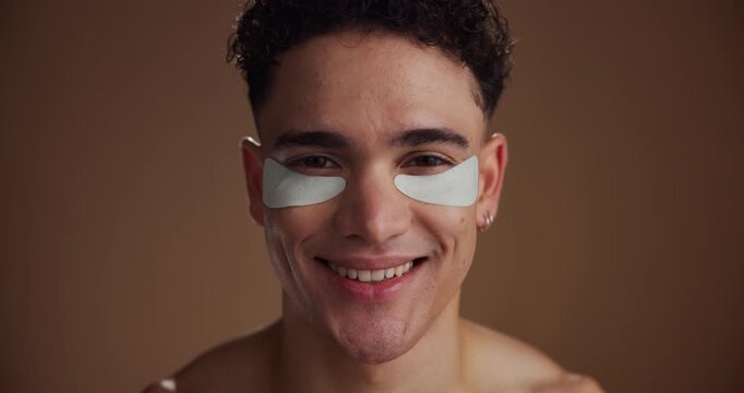 Face, eye patches and man with cosmetics, smile and beauty on brown studio background. Portrait, space and happy person with dermatology, spa wellness or grooming with routine, aesthetic or treatment